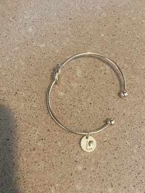 Gold tone bangle bracelet with L charm and infinity twist